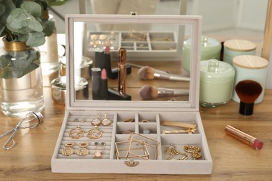 Elegant jewelry box with beautiful bijouterie, cosmetics and candles on wooden table