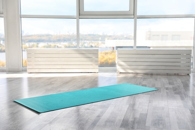 Photo of Unrolled light blue yoga mat on floor in room