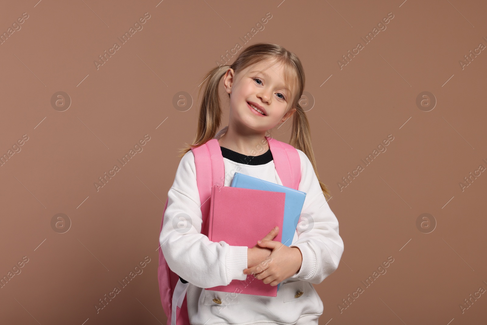 Photo of Happy schoolgirl with backpack and books on brown background