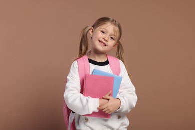 Happy schoolgirl with backpack and books on brown background