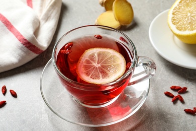 Photo of Glass cup of healthy goji tea with lemon on grey table