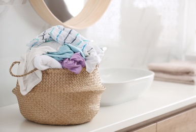 Photo of Wicker basket with dirty clothes on countertop in bathroom. Space for text