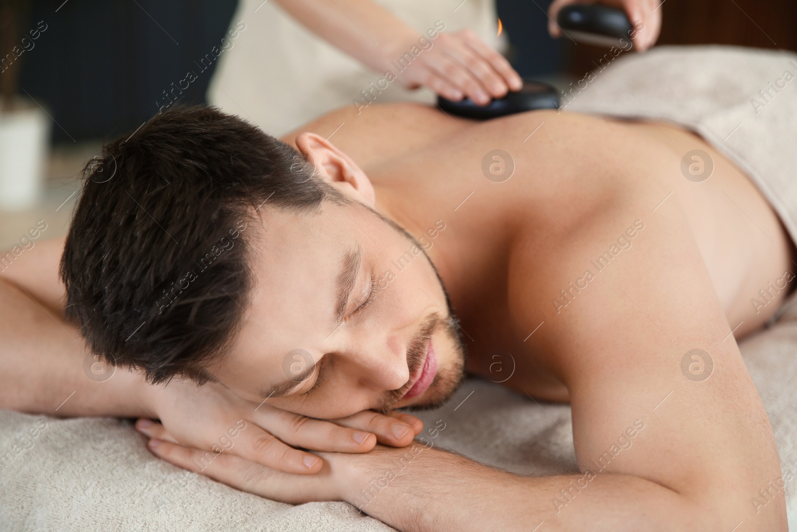 Photo of Handsome man receiving hot stone massage in spa salon