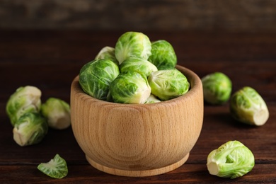 Photo of Bowl with fresh Brussels sprouts on brown wooden table, closeup