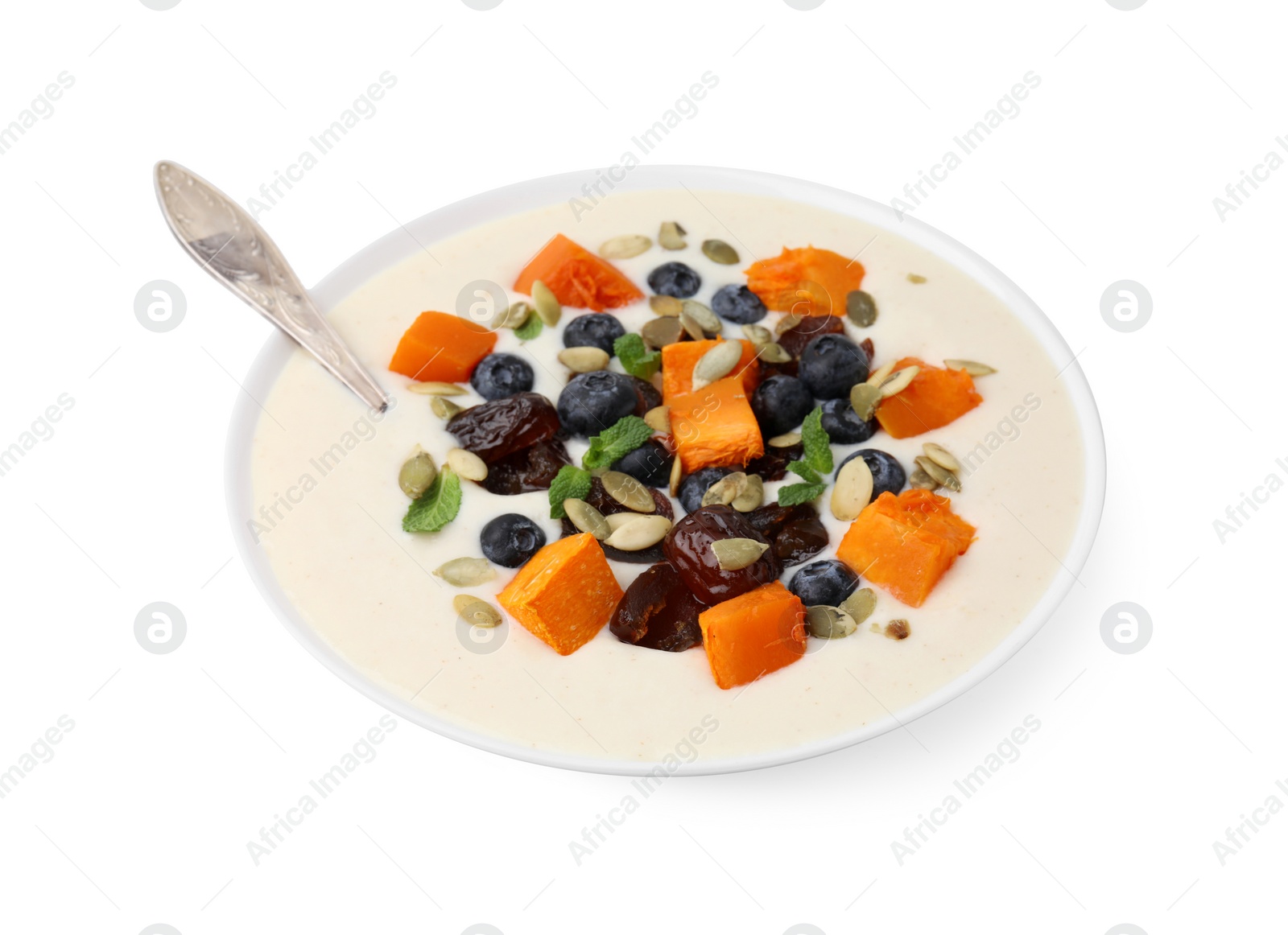 Photo of Delicious semolina pudding with blueberries, dates, pumpkin, mint and spoon in bowl isolated on white