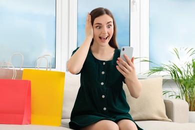 Special Promotion. Emotional young woman looking at smartphone on sofa indoors