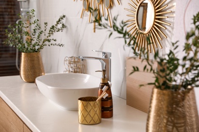 Photo of Vase with beautiful branches and toiletries near vessel sink in bathroom. Interior design