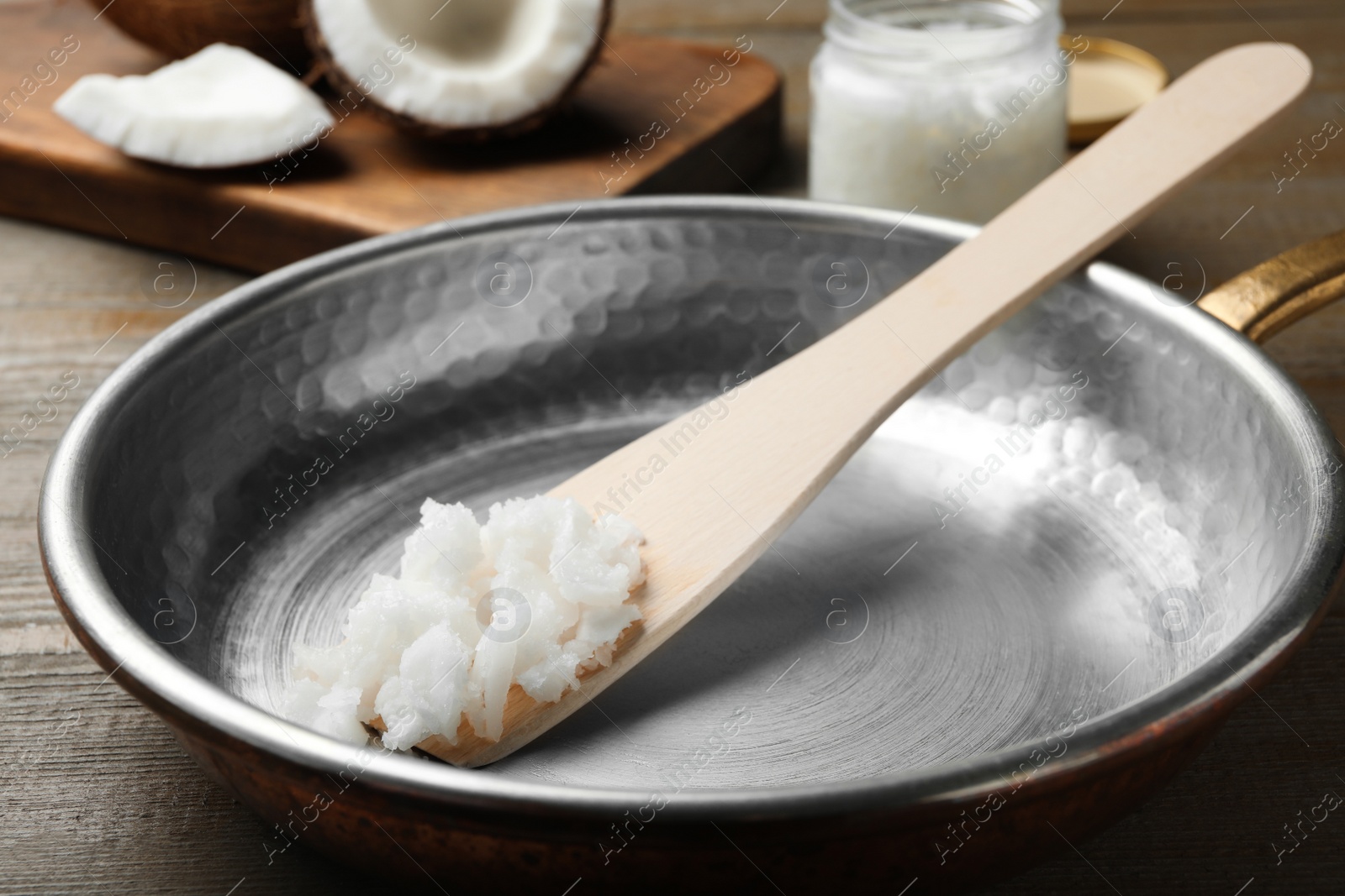 Photo of Frying pan with coconut oil and wooden spatula on wooden table, closeup. Healthy cooking