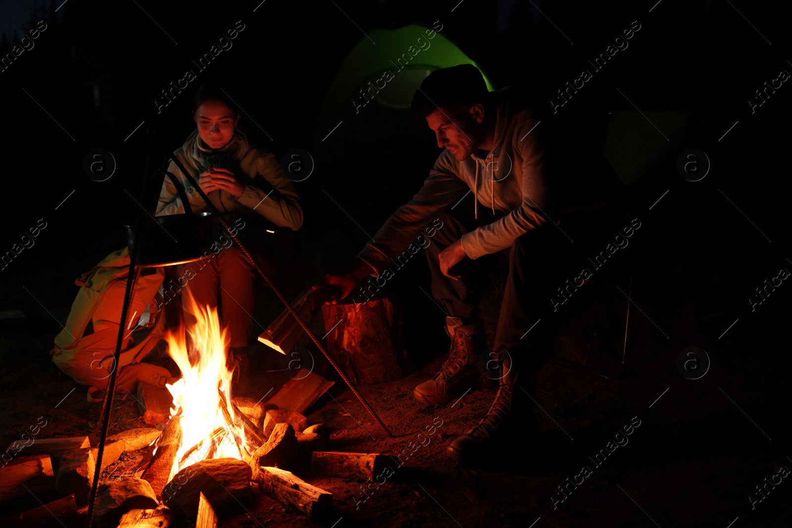 Photo of Couple sitting near bonfire in camp at night