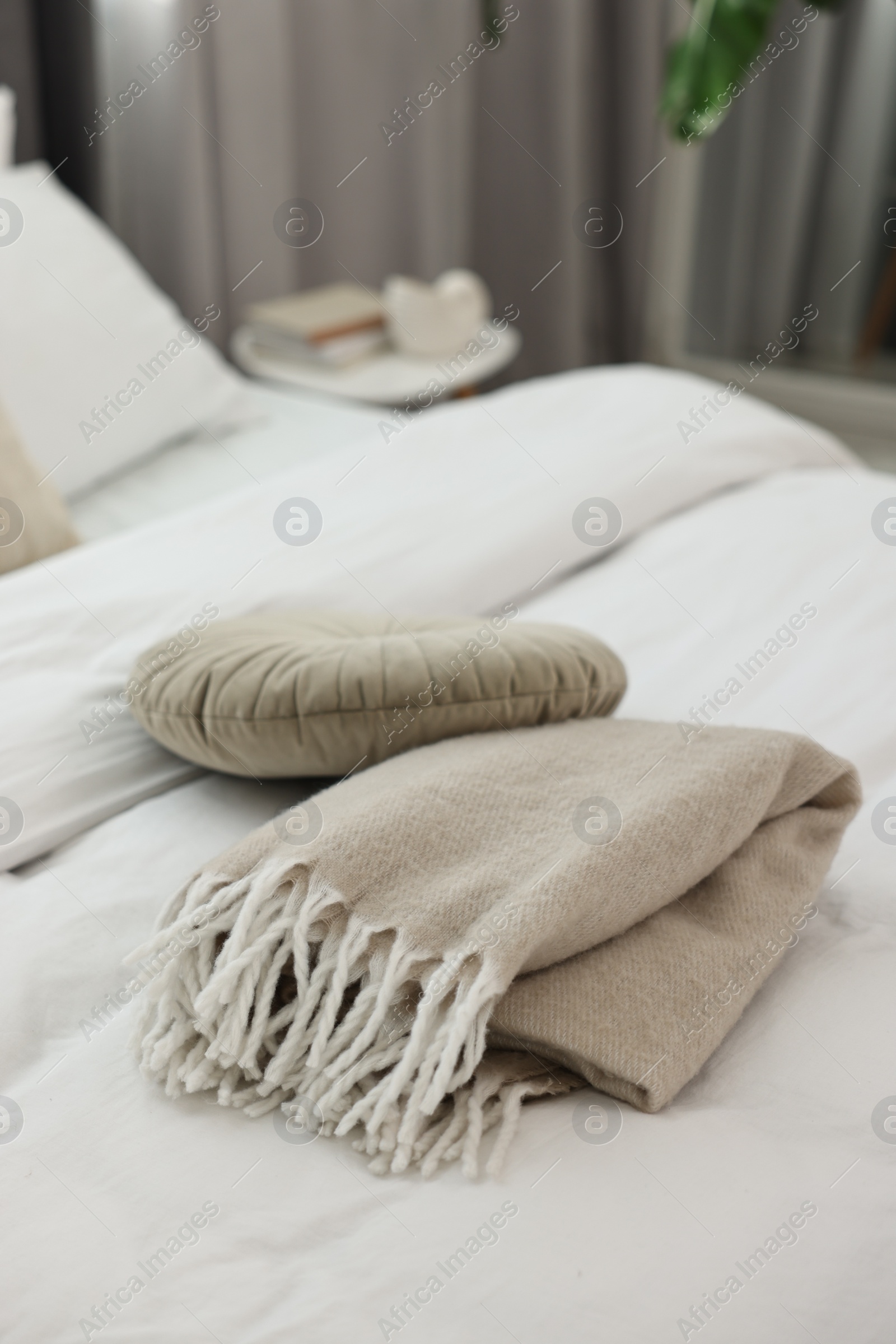 Photo of Soft beige plaid and pillow on bed in room