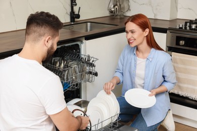 Photo of Lovely couple loading dishwasher with plates in kitchen