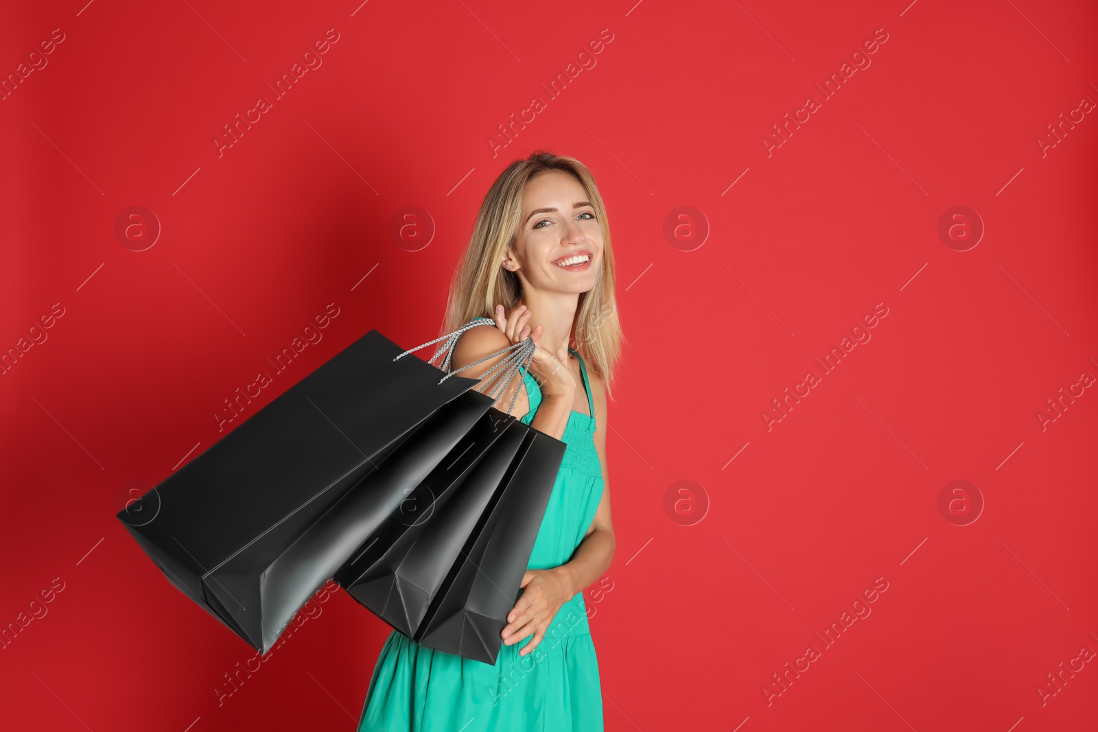 Photo of Happy young woman with shopping bags on red background, space for text. Black Friday Sale