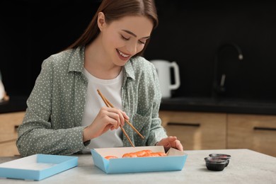 Photo of Beautiful young woman eating sushi rolls with chopsticks at table in kitchen