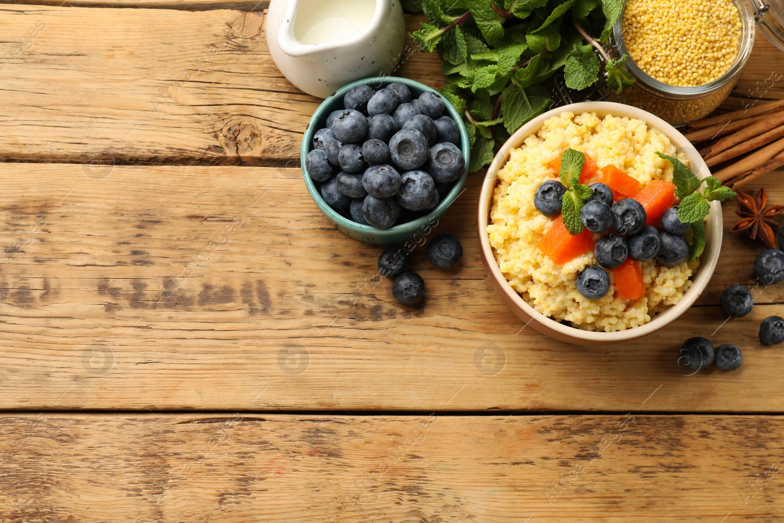 Photo of Tasty millet porridge with blueberries, pumpkin and mint in bowl on wooden table, flat lay. Space for text