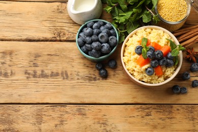 Photo of Tasty millet porridge with blueberries, pumpkin and mint in bowl on wooden table, flat lay. Space for text