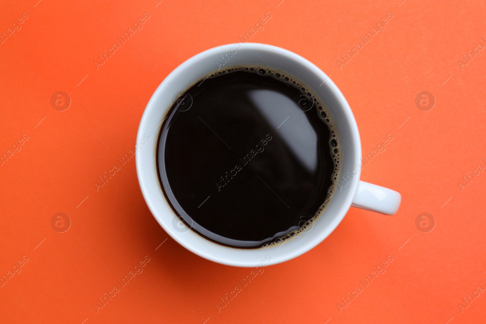 Photo of White mug of freshly brewed hot coffee on orange background, top view