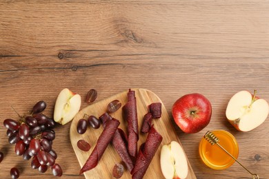 Flat lay composition with delicious fruit leather rolls on wooden table. Space for text