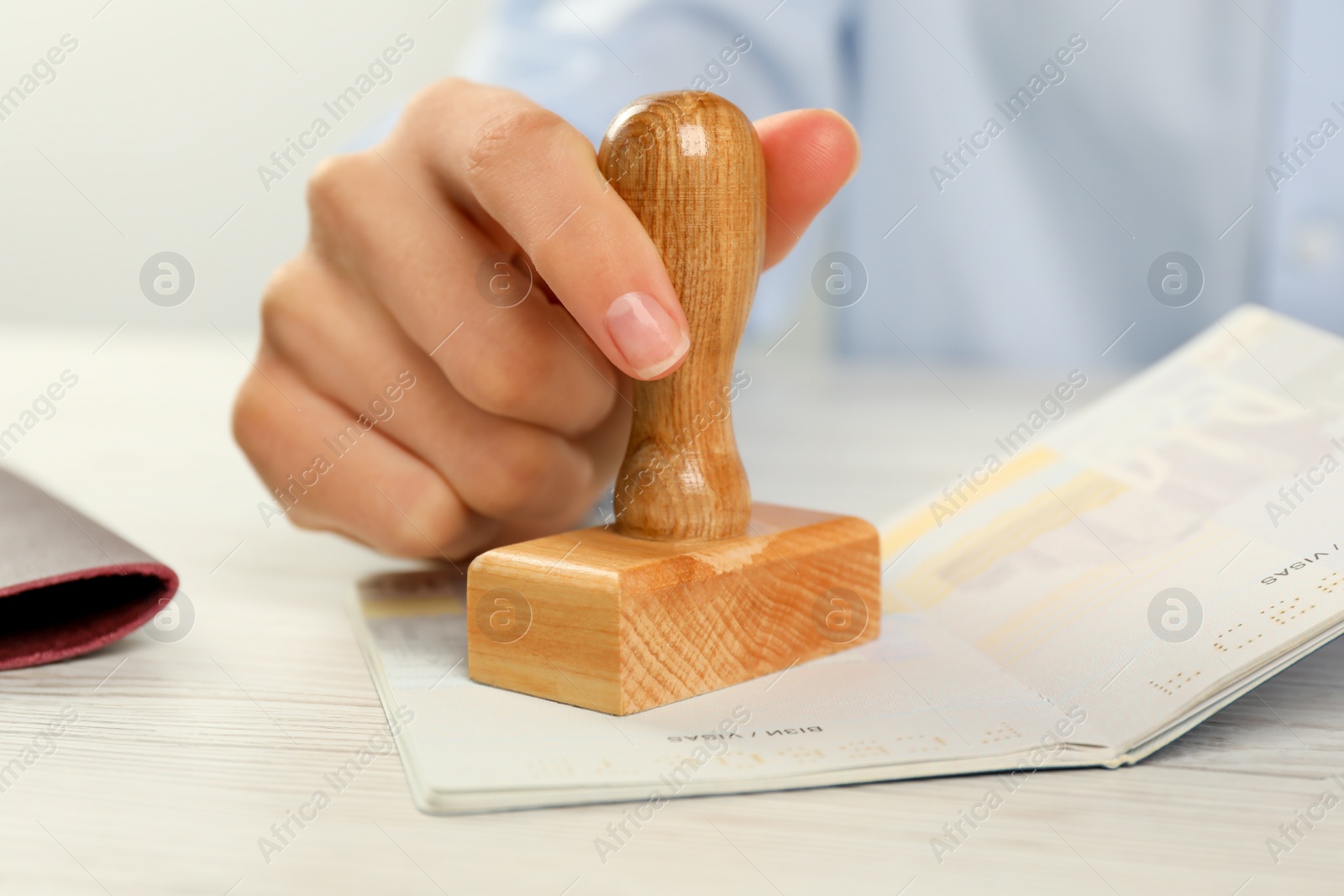 Photo of Moldova, Ceadir-Lunga - June 13, 2022: Woman stamping visa page in passport at white wooden table, closeup