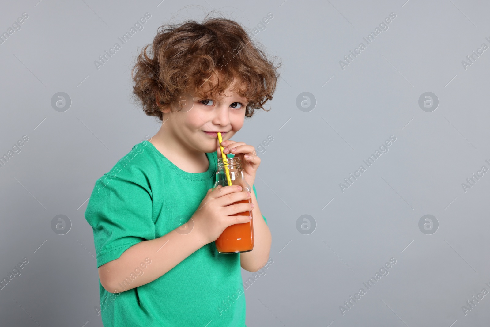 Photo of Cute little boy drinking fresh juice through straw on light gray background, space for text