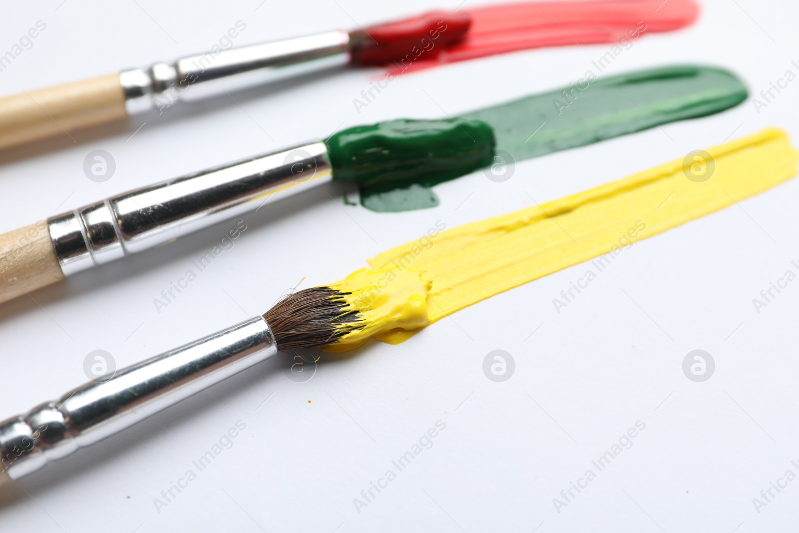 Photo of Brushes with different paints and strokes on white background, closeup