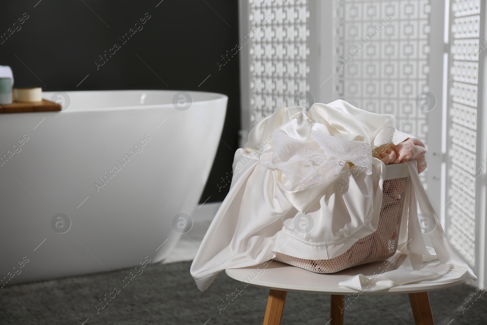 Photo of Laundry basket filled with clothes on table in bathroom. Space for text