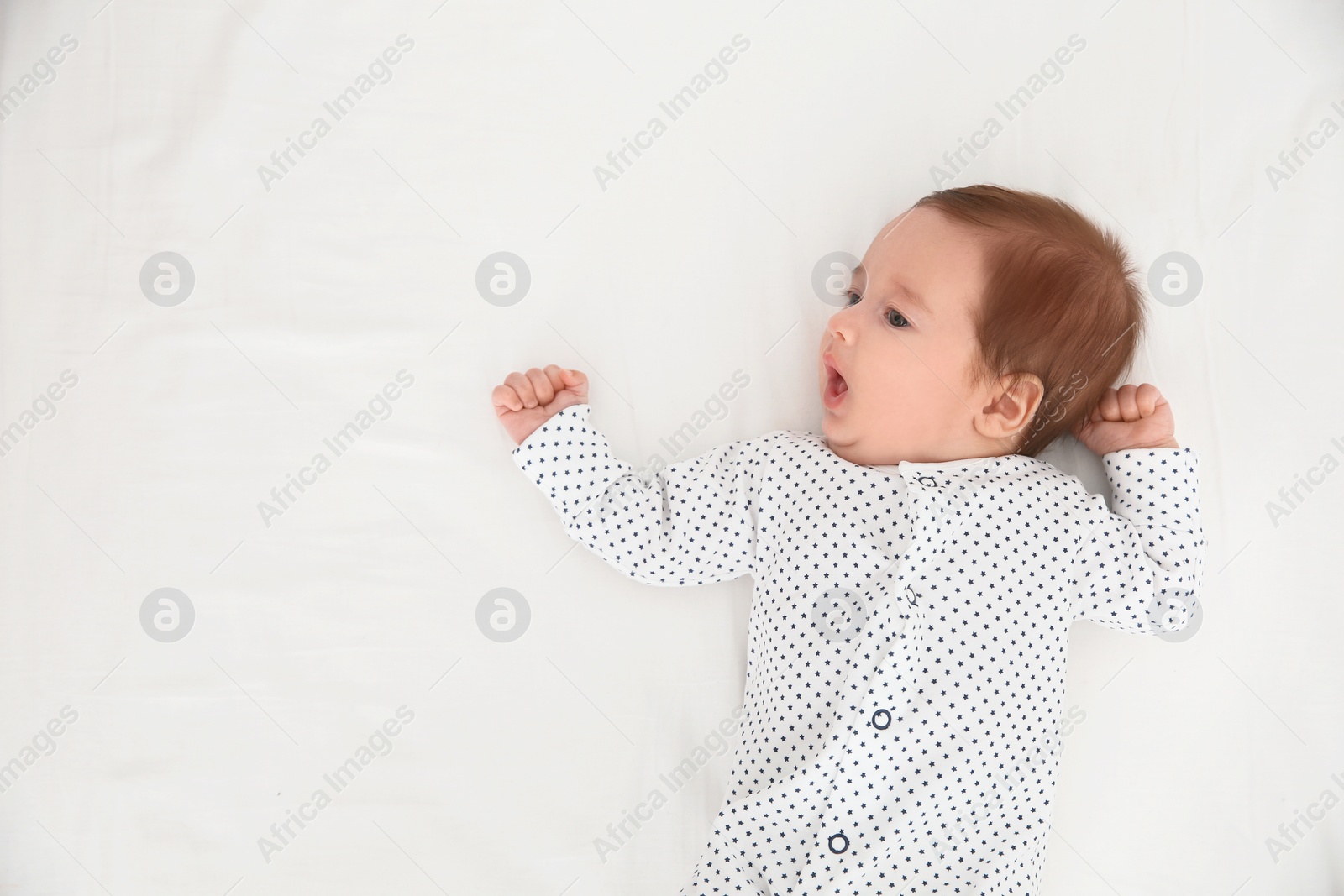 Photo of Adorable baby on white sheet, top view. Space for text