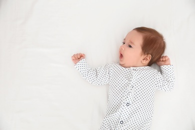 Adorable baby on white sheet, top view. Space for text