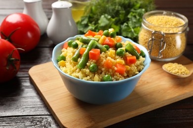 Photo of Tasty millet porridge with vegetables in bowl on wooden table, closeup