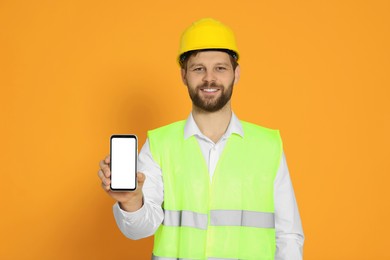 Photo of Man in reflective uniform showing smartphone on orange background
