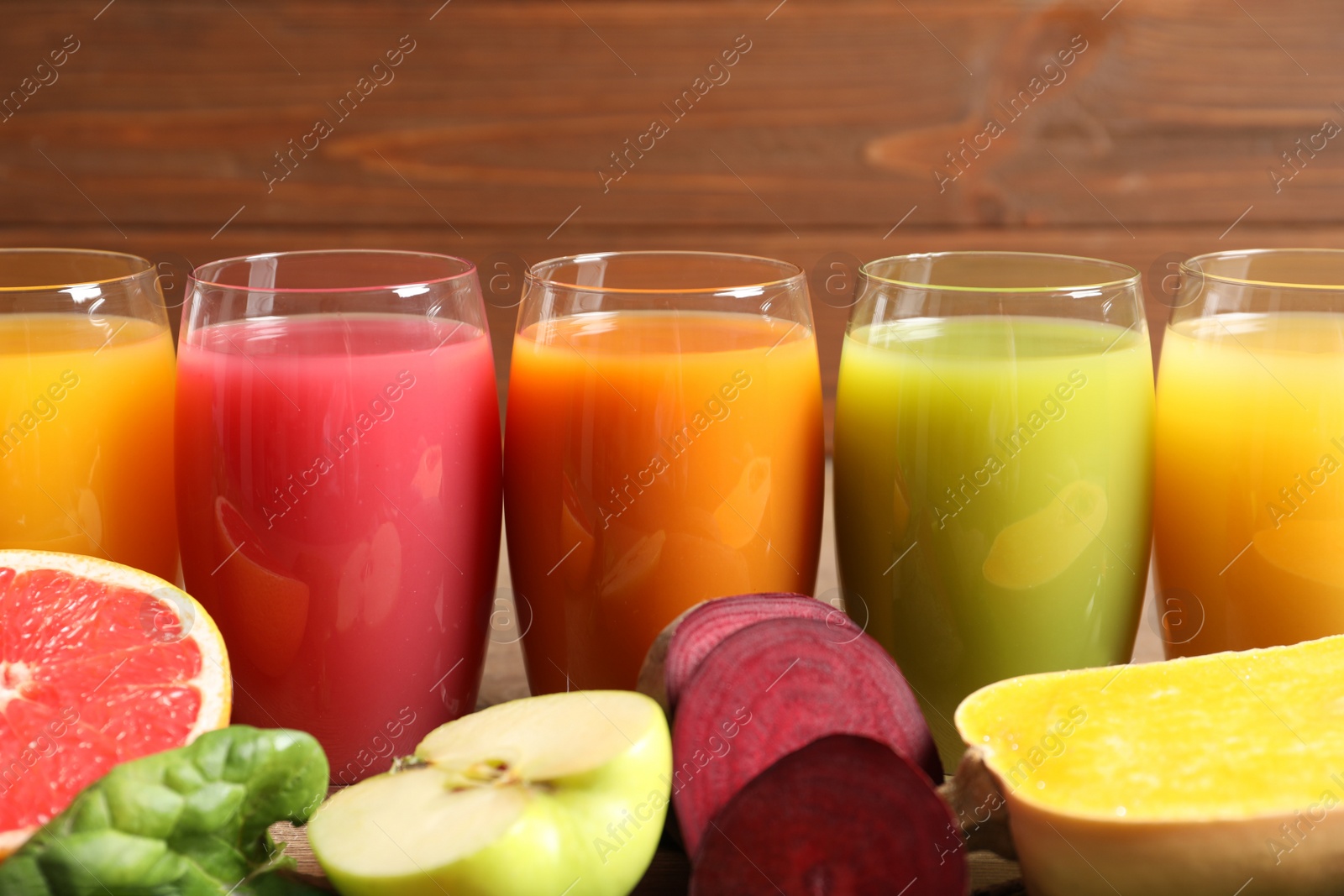 Photo of Glasses with different juices and fresh ingredients on wooden background