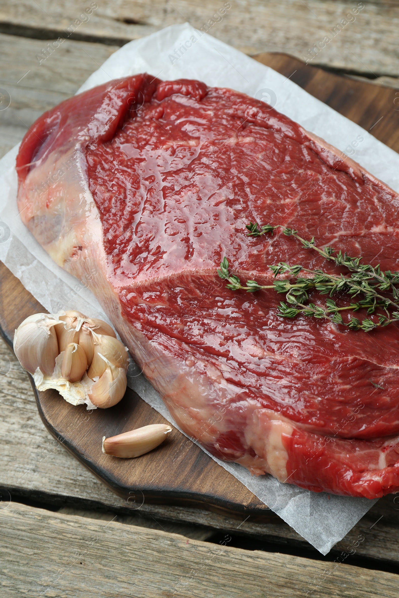 Photo of Piece of raw meat, garlic and thyme on wooden table, closeup