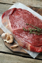 Piece of raw meat, garlic and thyme on wooden table, closeup