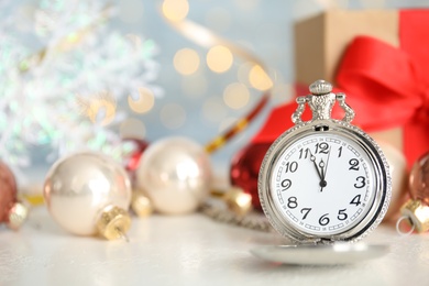 Photo of Pocket watch, gift and festive decor on table against blurred lights. New Year countdown