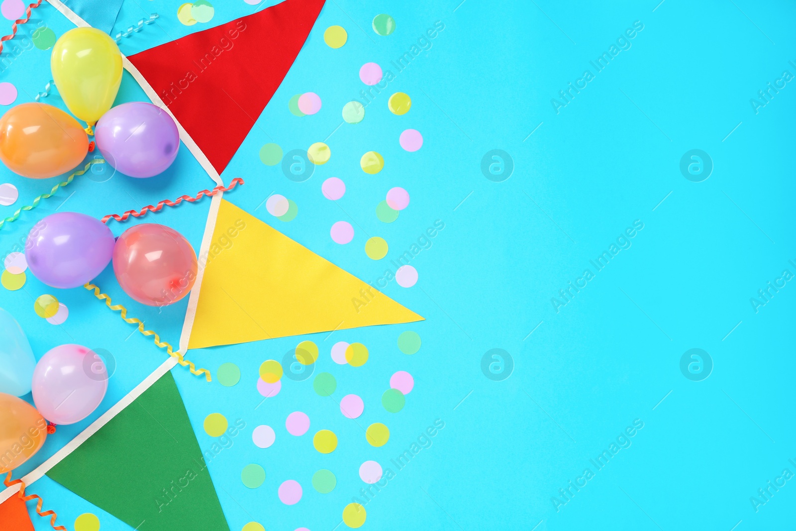 Photo of Bunting with colorful triangular flags, balloons, streamers and confetti on light blue background, flat lay. Space for text