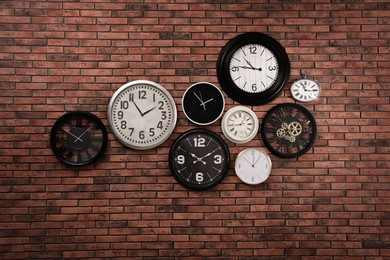 Photo of Collection of clocks hanging on red brick wall