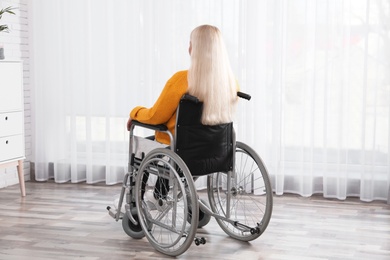 Photo of Mature woman sitting in wheelchair near window at home
