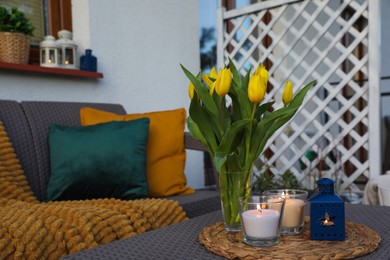 Photo of Soft pillows, blanket, burning candles and yellow tulips on rattan garden furniture outdoors