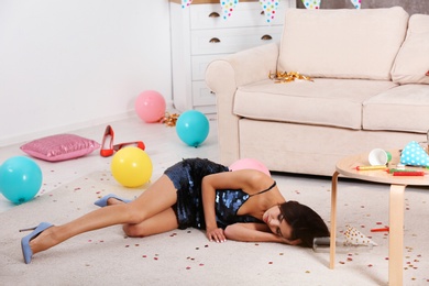 Photo of Young woman sleeping on floor in messy room after party