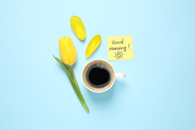 Photo of Delicious coffee, tulip and card with GOOD MORNING wish on light blue background, flat lay