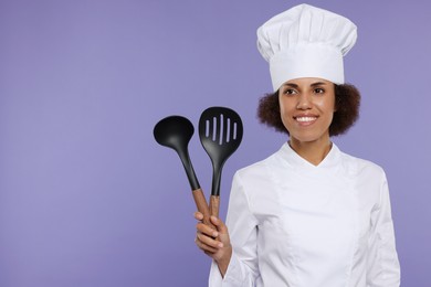Photo of Happy female chef in uniform holding skimmer and ladle on purple background. Space for text