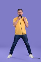 Handsome man with microphone singing on violet background