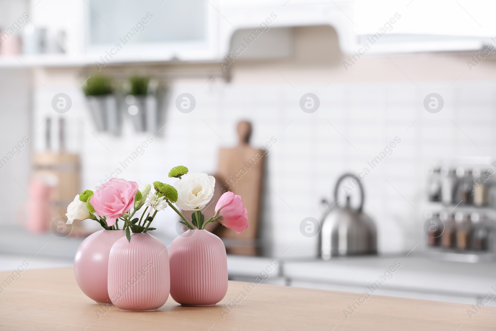 Photo of Vases with beautiful flowers on table in kitchen interior. Space for text