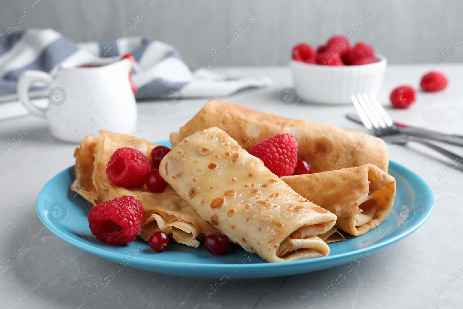 Photo of Delicious crepes served with berries on light grey table, closeup