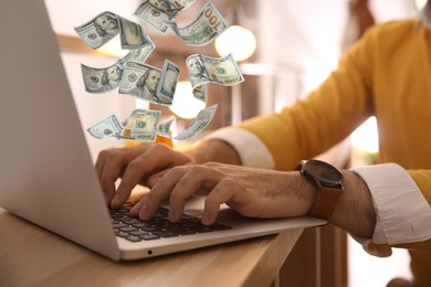 Image of Making money online. Closeup view of man using laptop at table and flying dollars