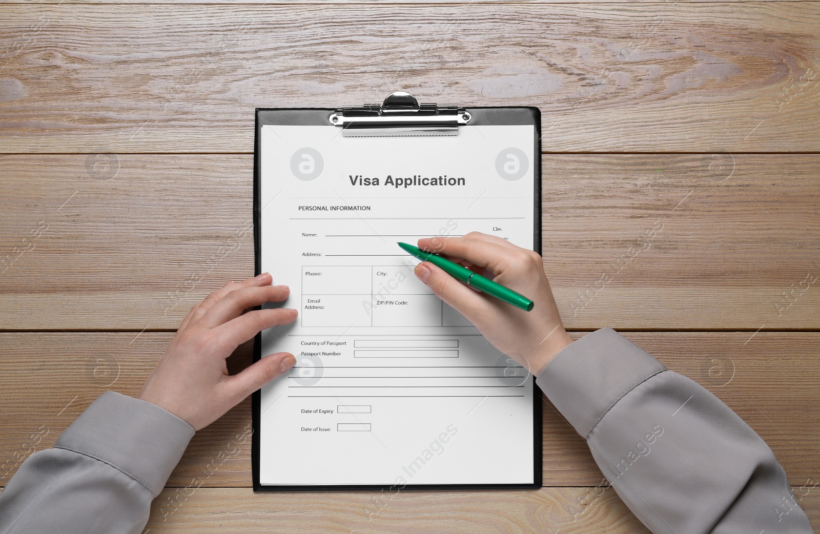 Photo of Woman filling visa application form at wooden table, top view