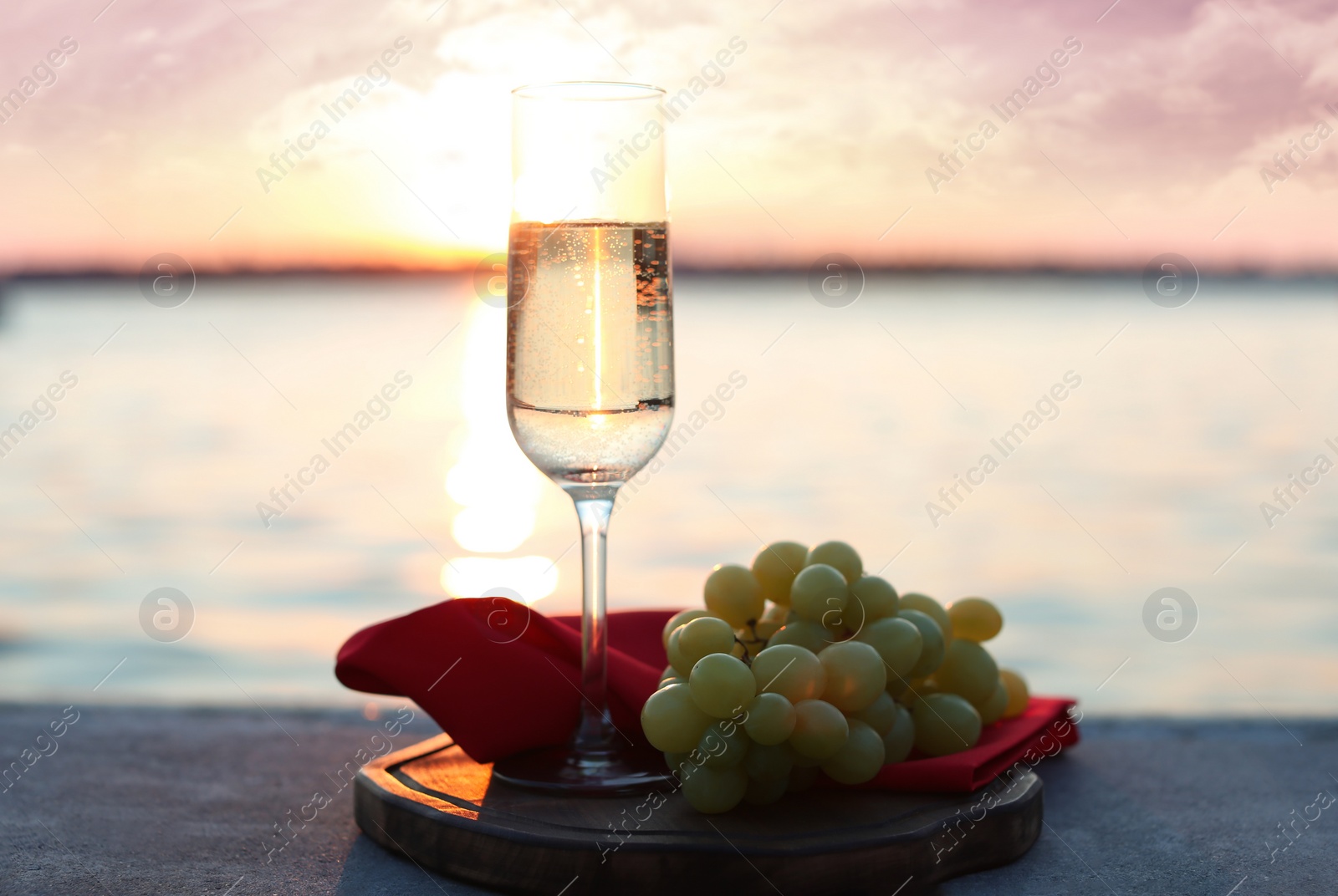 Photo of Glass of champagne and and fresh grapes served near river at sunset