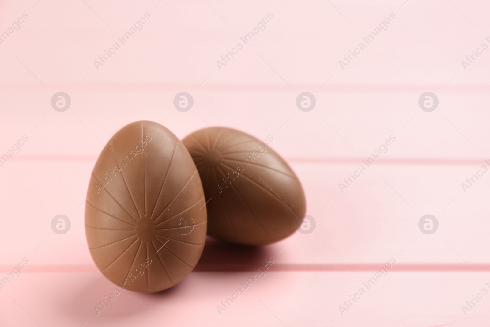 Photo of Sweet chocolate eggs on pink wooden table. Space for text