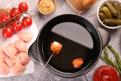 Fondue pot, forks with fried meat pieces, tomatoes and other products on grey textured table, flat lay