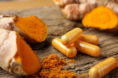 Aromatic turmeric powder, raw roots and pills on wooden surface, closeup