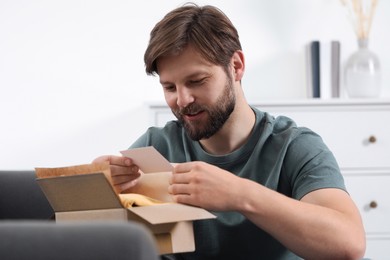 Photo of Happy man with greeting card near parcel at home. Internet shopping